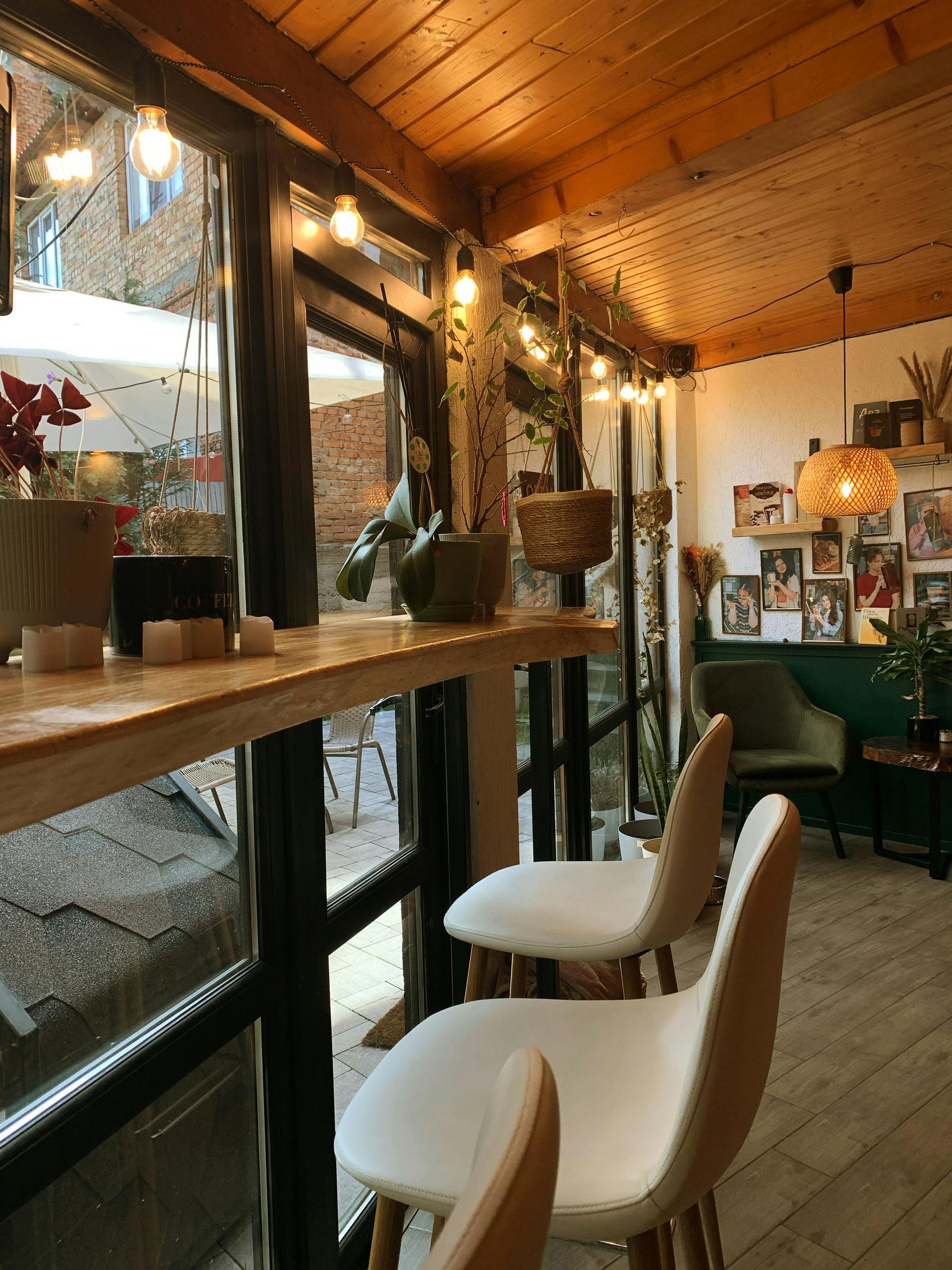 Cozy cafe corner with bar seating, string lights, plants, and a window view.