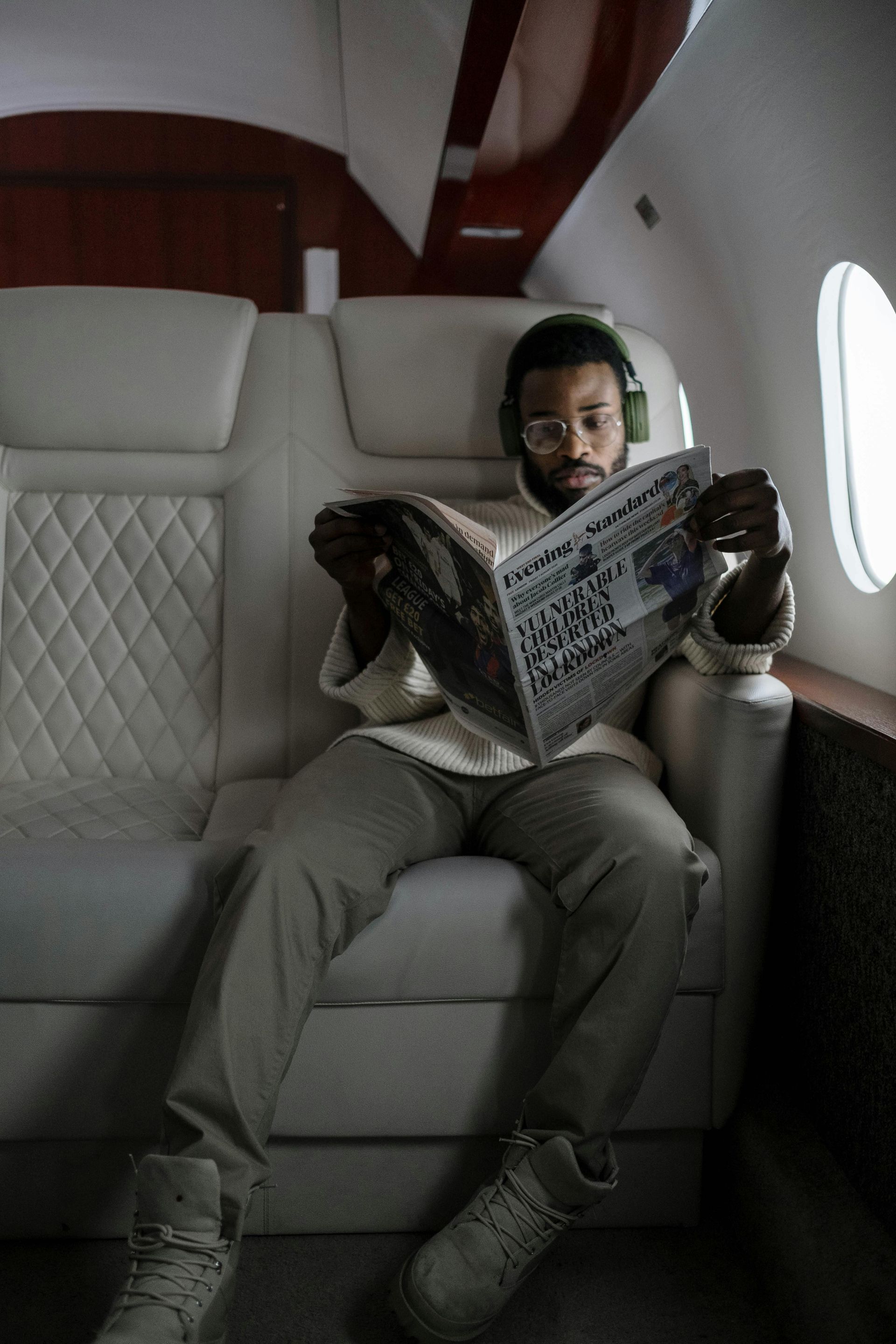 Person wearing headphones reads newspaper inside a private jet.