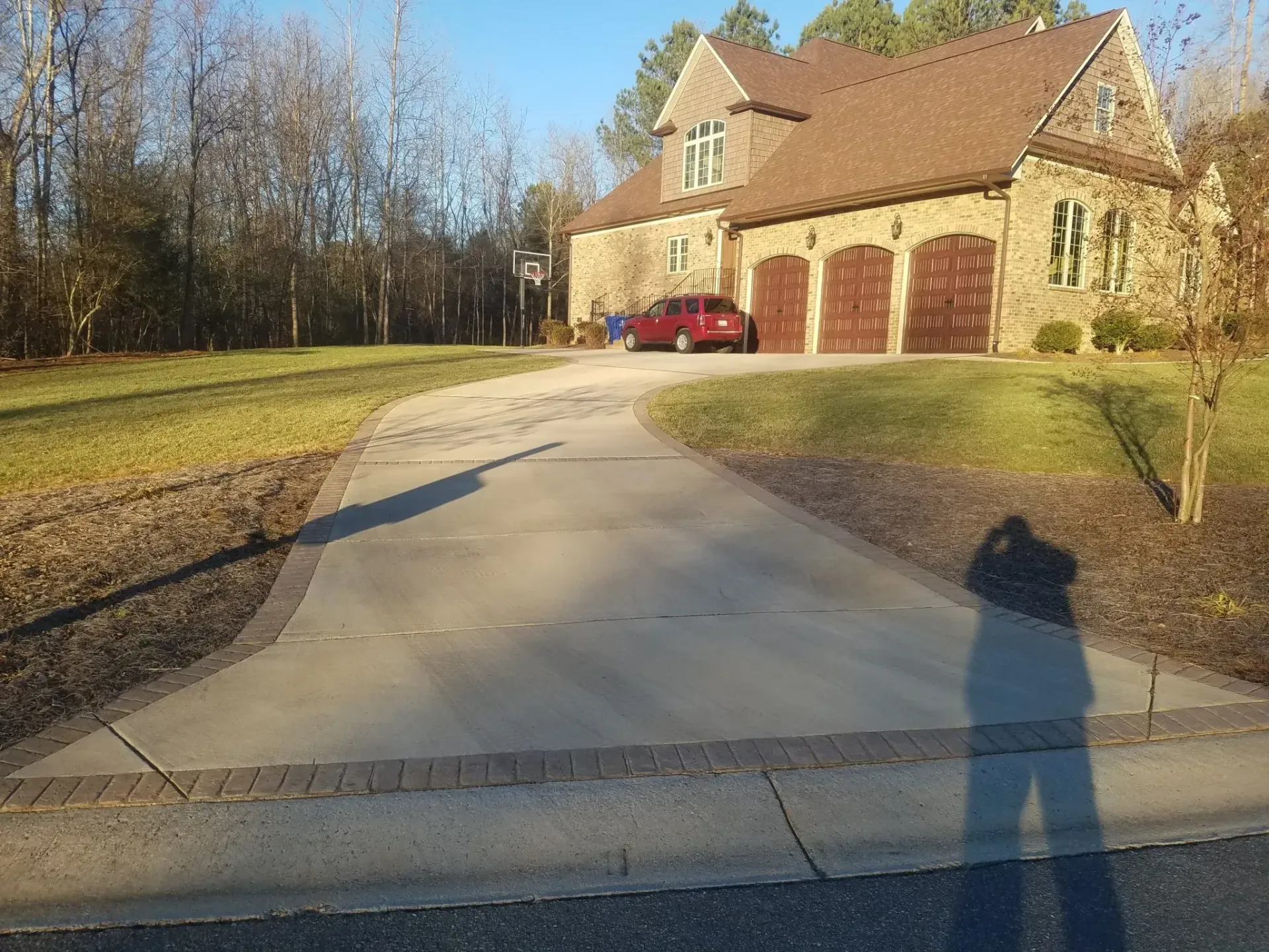 Driveway leading to a stone house with red garage doors, a red car, and long shadows in late afternoon.