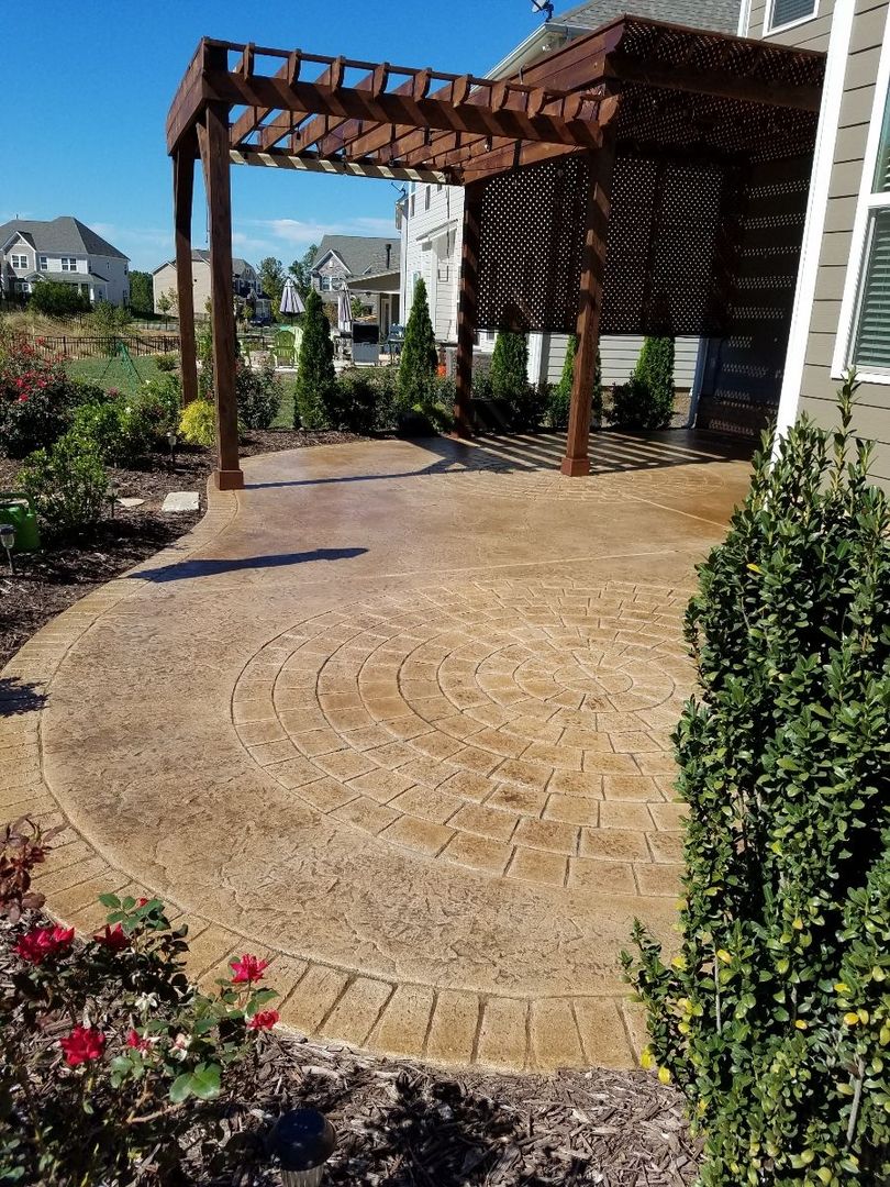 Backyard patio with stamped concrete, a wooden pergola, and surrounding garden plants