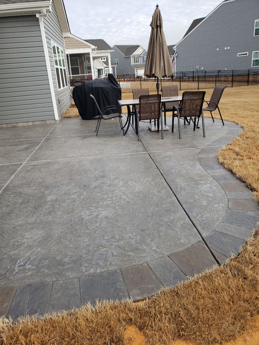 Back patio with stone pavers, outdoor dining table, closed umbrella, and grill beside houses