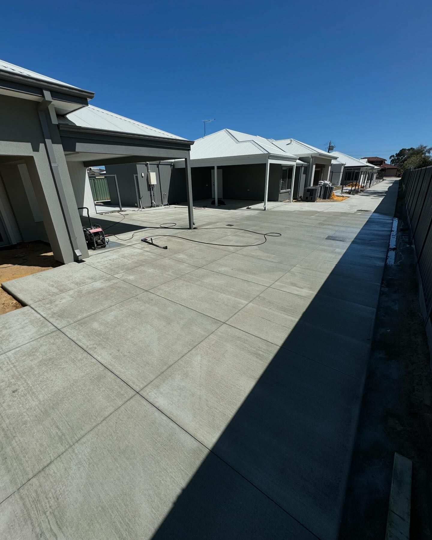 Newly constructed row of houses with concrete driveways under a clear blue sky.