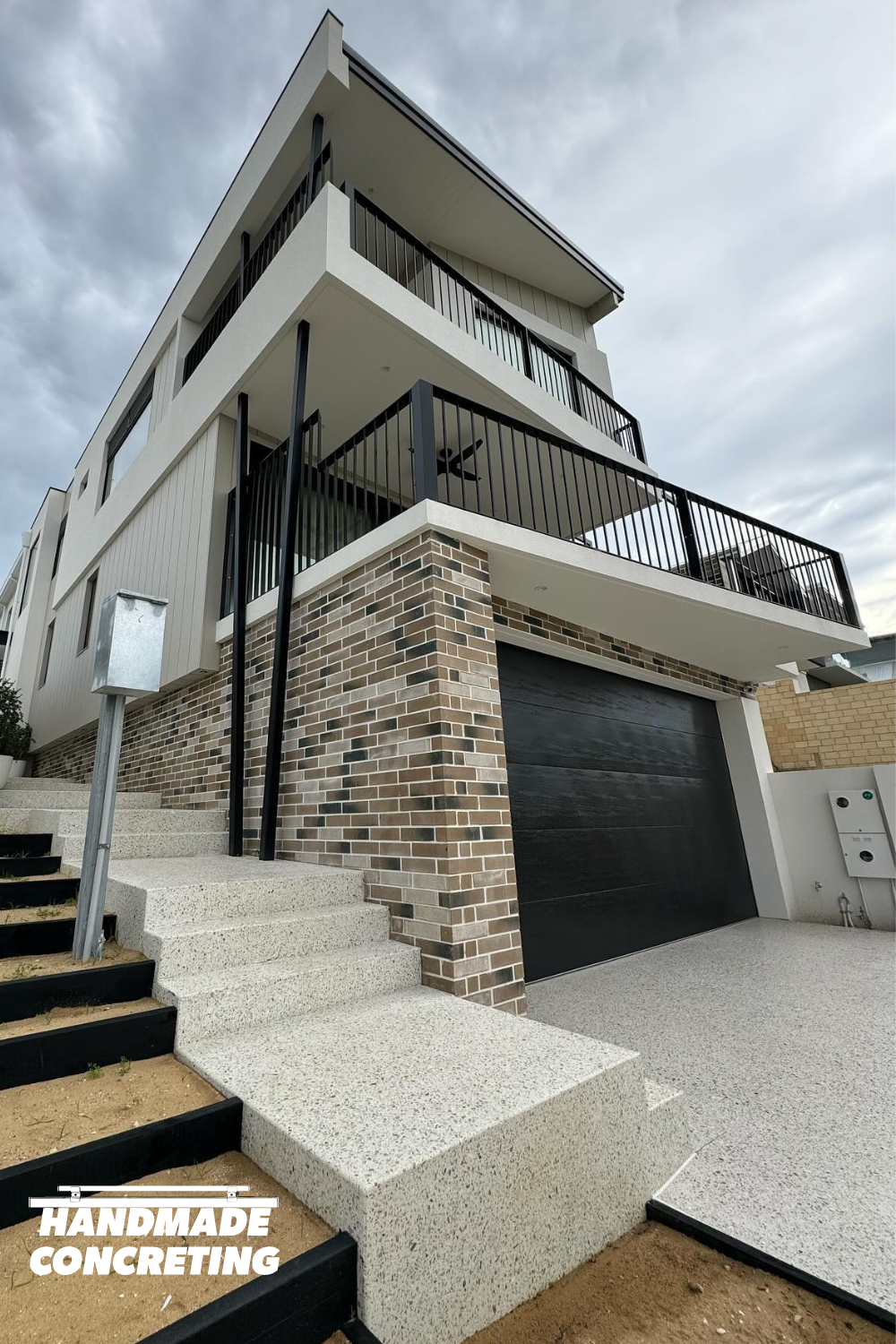 Exposed aggregate driveway with concrete pathway and stairs in architecturally designed home