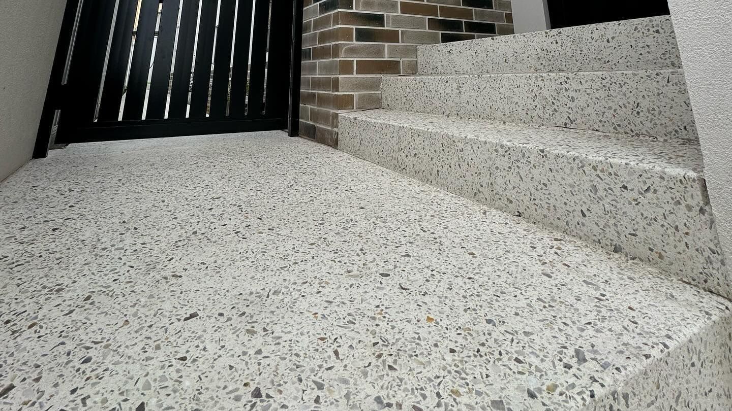 honed concrete floor and steps lead to a dark gate. Brick wall visible.