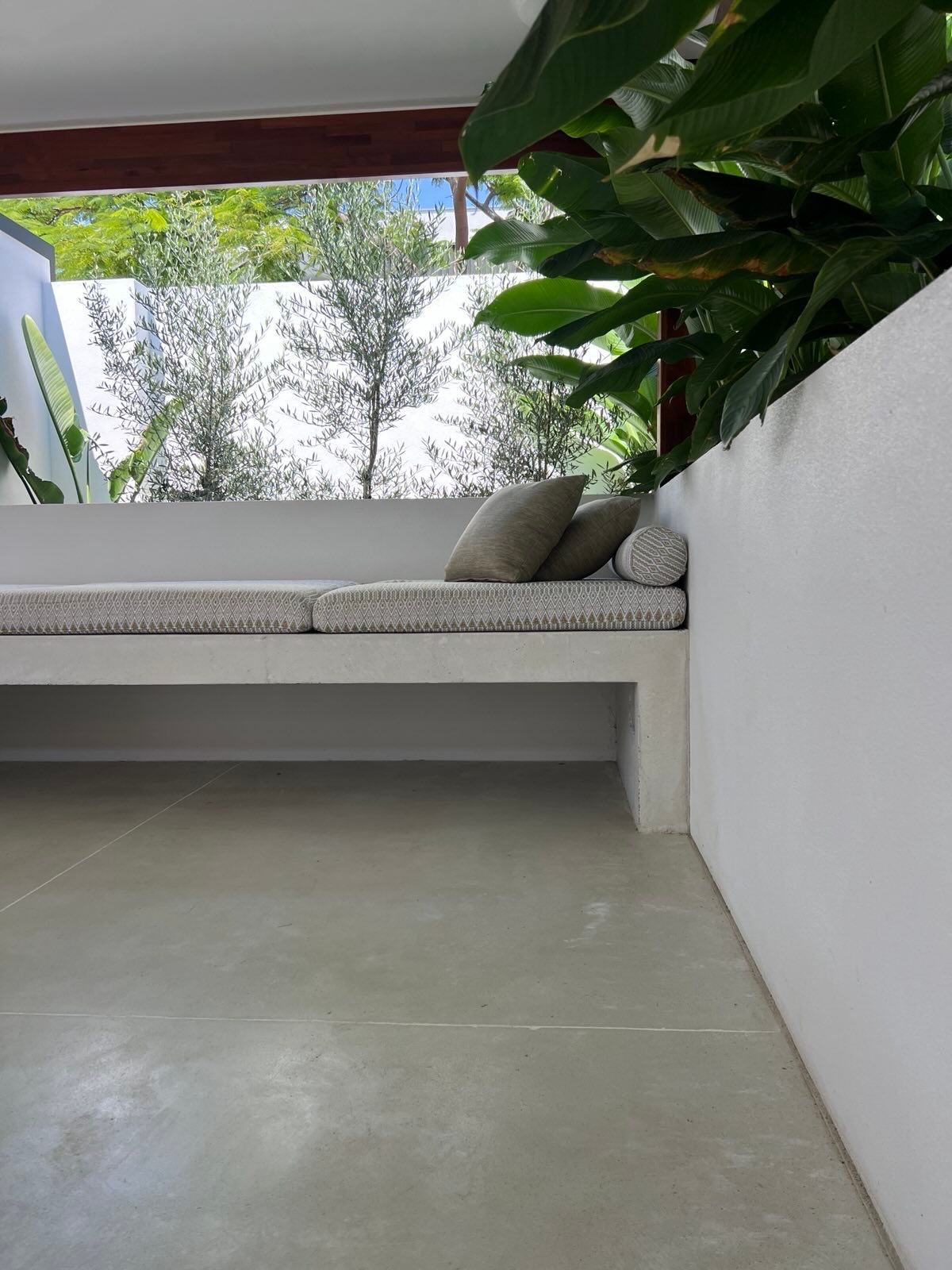 Built-in white outdoor concrete bench with patterned cushions and pillows overlooking trees.