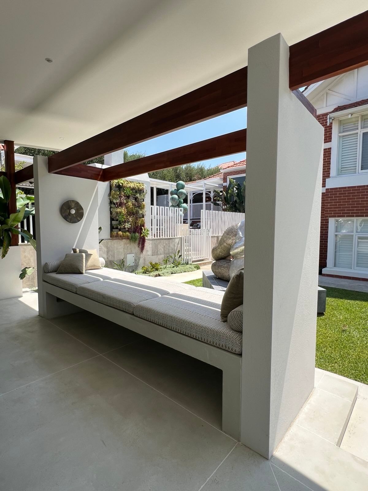 Outdoor concrete seating area with a built-in bench, pillows, and a living wall, under a pergola.