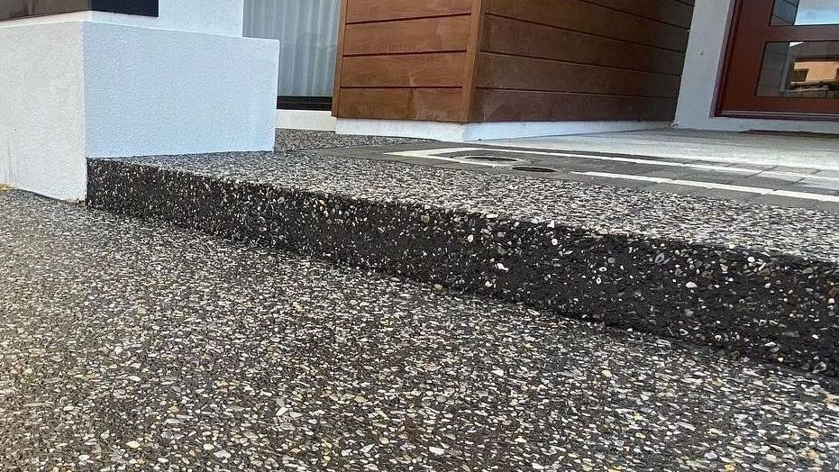 A close up of a exposed aggregate concrete walkway with steps leading up to a house.