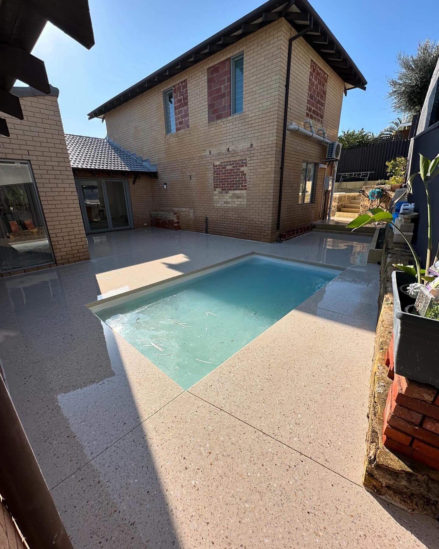 A large house with a swimming pool in front of it and honed concrete pool surrounds