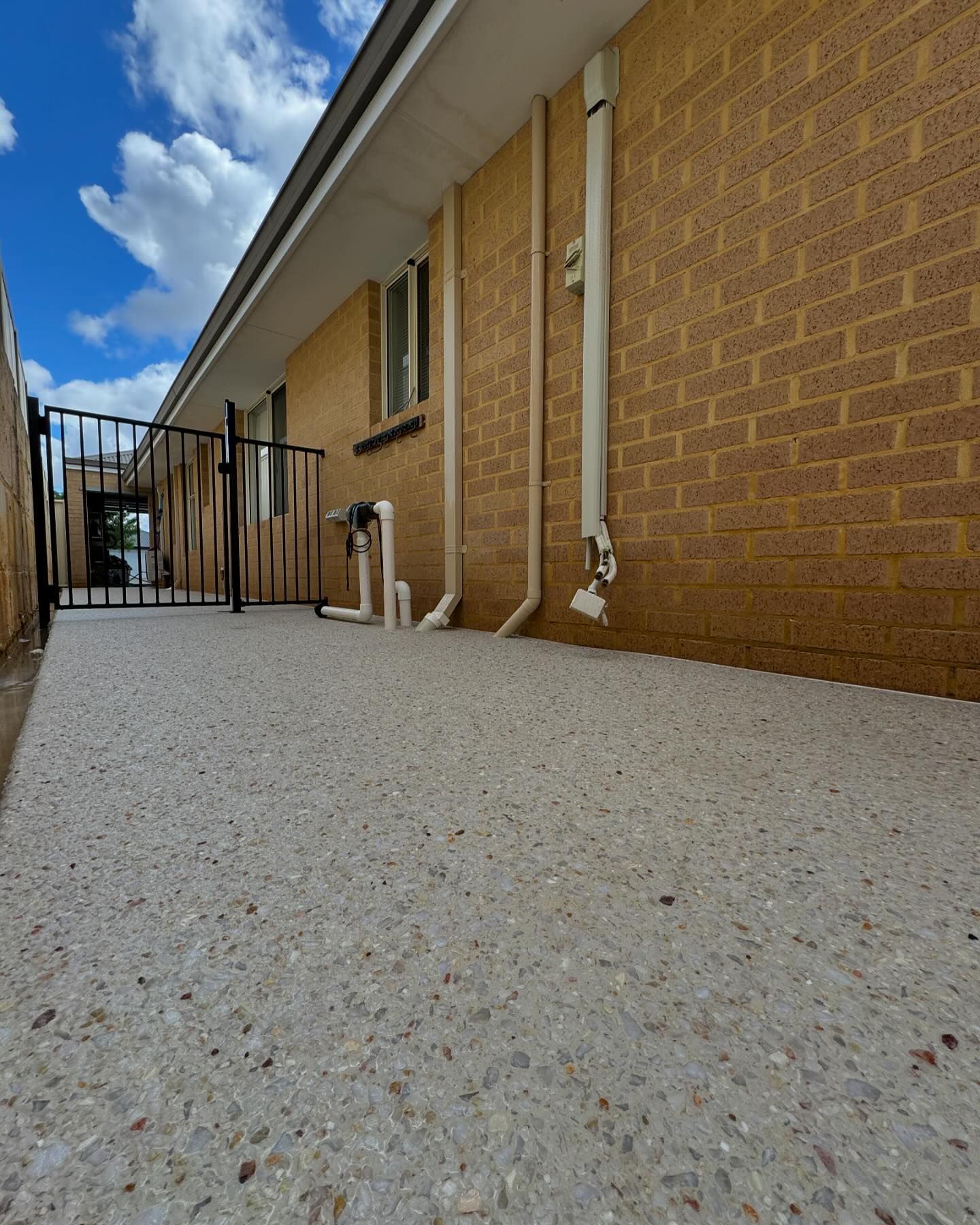 White exposed aggregate concrete against brick wall running down the side of a house,