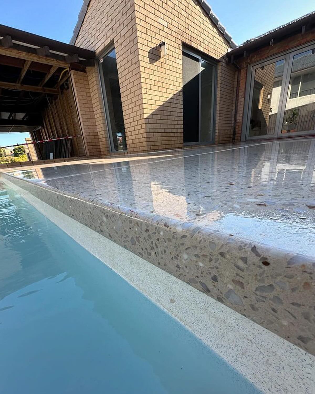 A brick house with a swimming pool in front of it and honed concrete pool area.