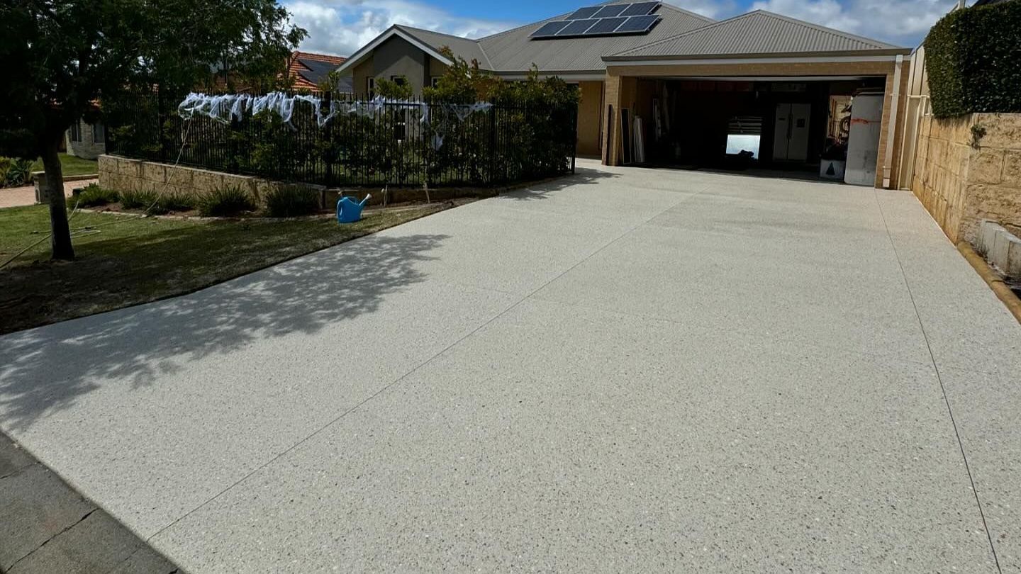 Driveway with exposed aggregate and surrounding it is green grass and gardens