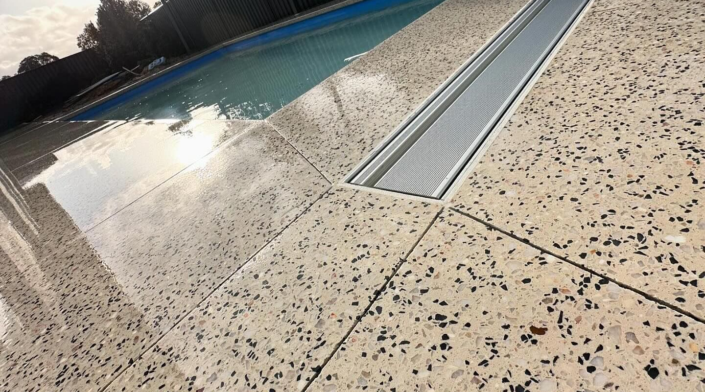 Sealed Coral White Honed concrete around newly installed pool featuring embedded grate for drainage.