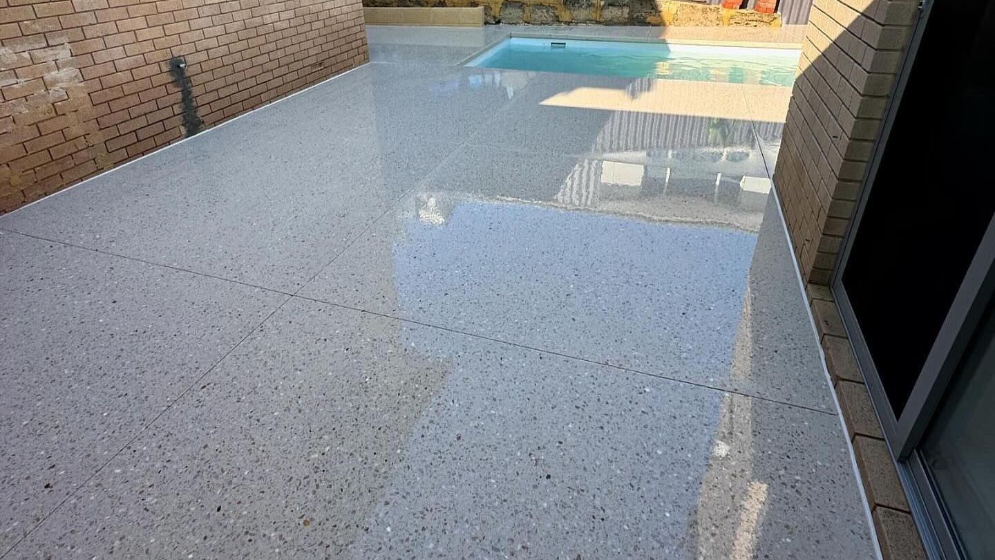 A patio with a swimming pool in the background and honed aggregate concrete patio and pool area flooring