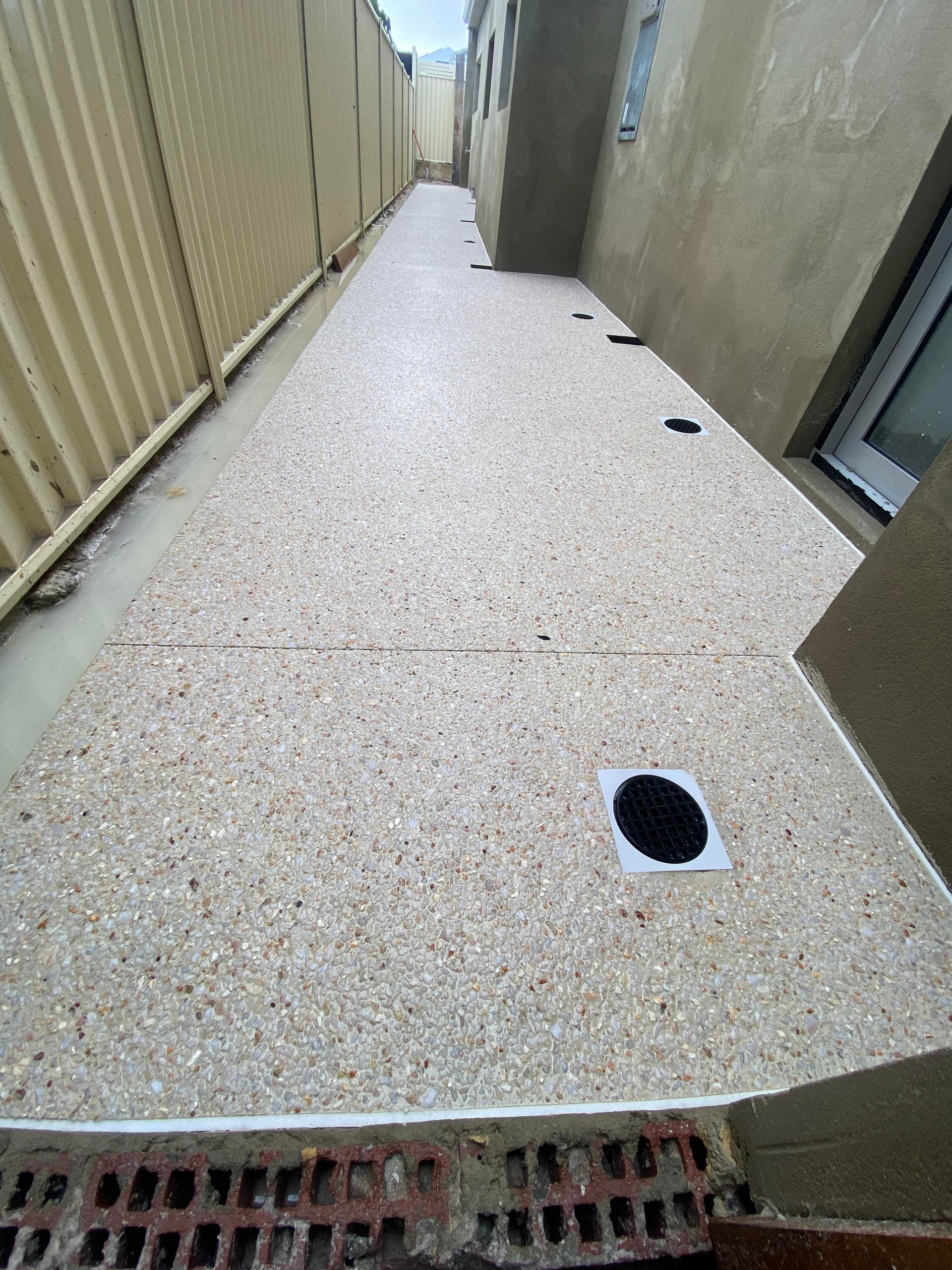 Exposed aggregate pathway running down the side of the house with drainage installed.