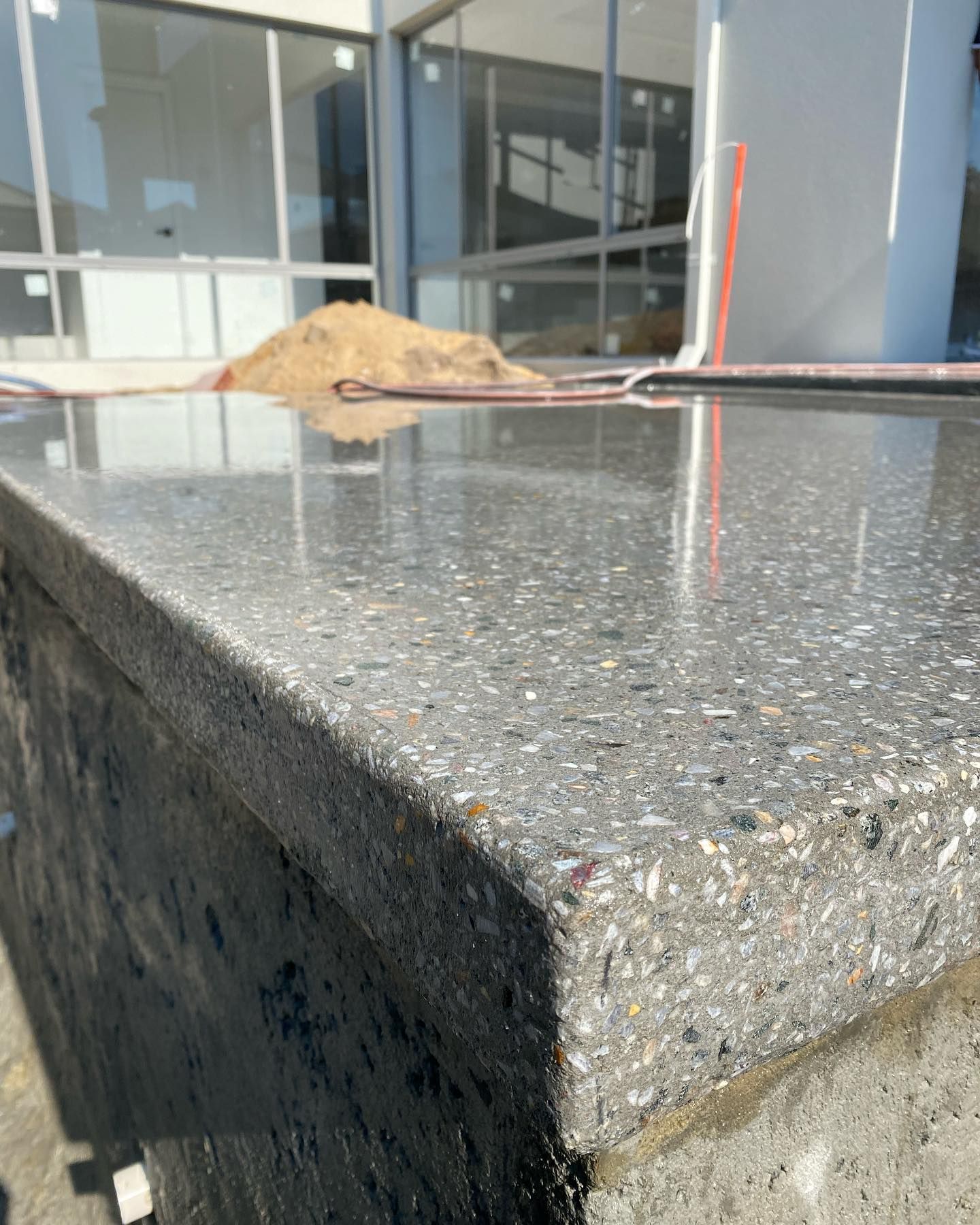 Close-up of a honed concrete surface; appears to be an outdoor countertop, with a pile of sand in the background.