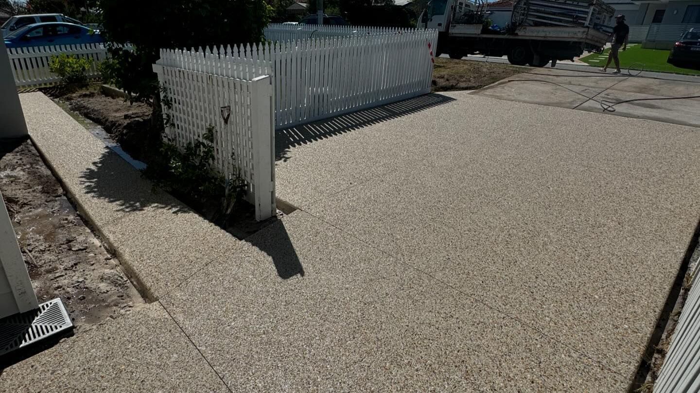 A concrete driveway with a white picket fence in the background.