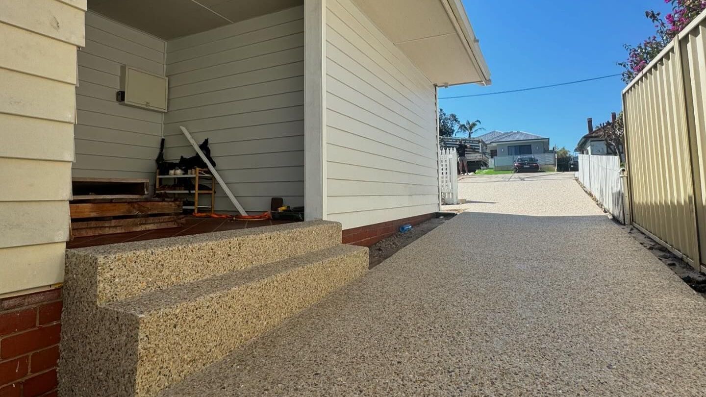 A white house with exposed aggregate stairs leading up to it and exposed agg driveway