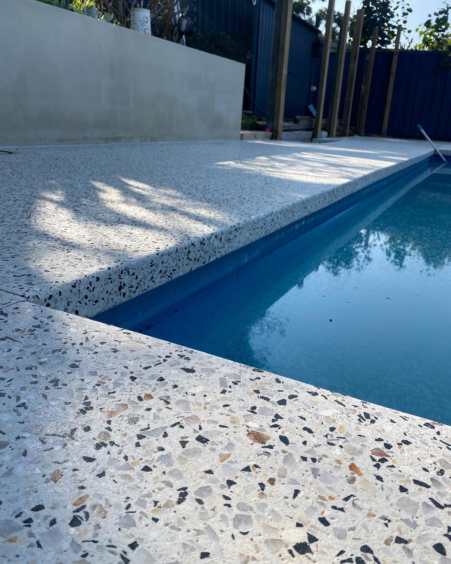 Honed concrete pool surrounds and pool edge with water in pool in Perth backyard. 