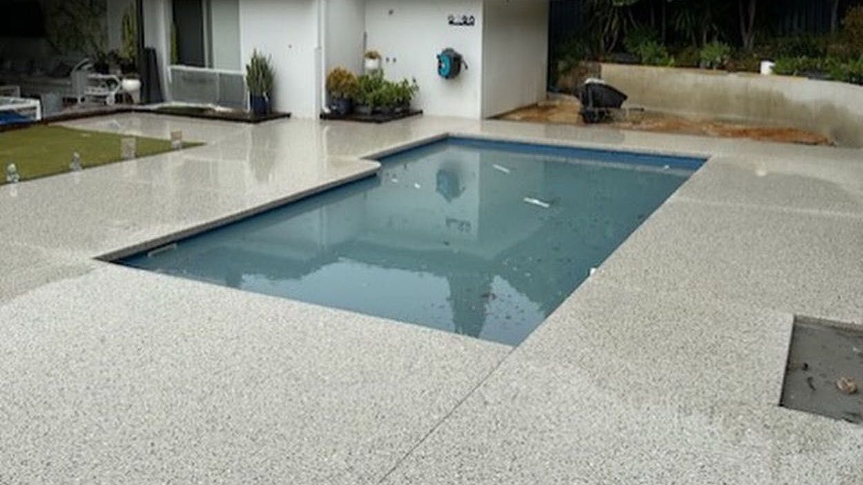 Honed Concrete Pool Surrounds with pool shed and grass in the background