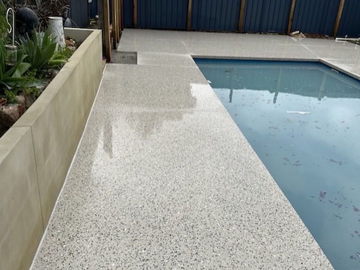 A swimming pool with honed concrete pool surrounds and a fence in the background