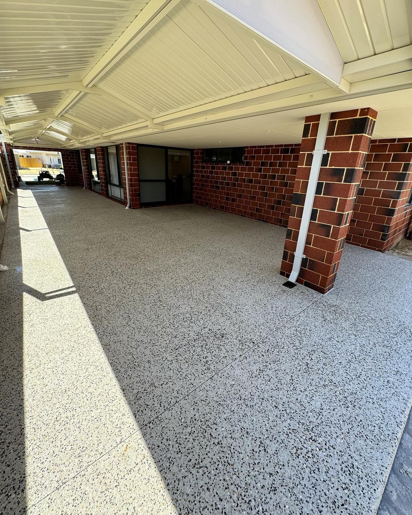 Exposed aggregate patio with down pipes and red brick house