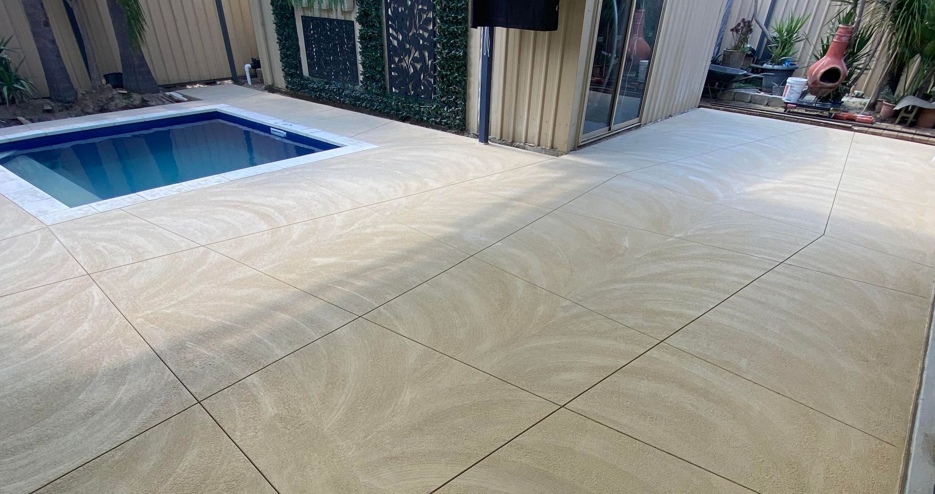 A patio with a swimming pool in the background and liquid limestone patio and pool area flooring