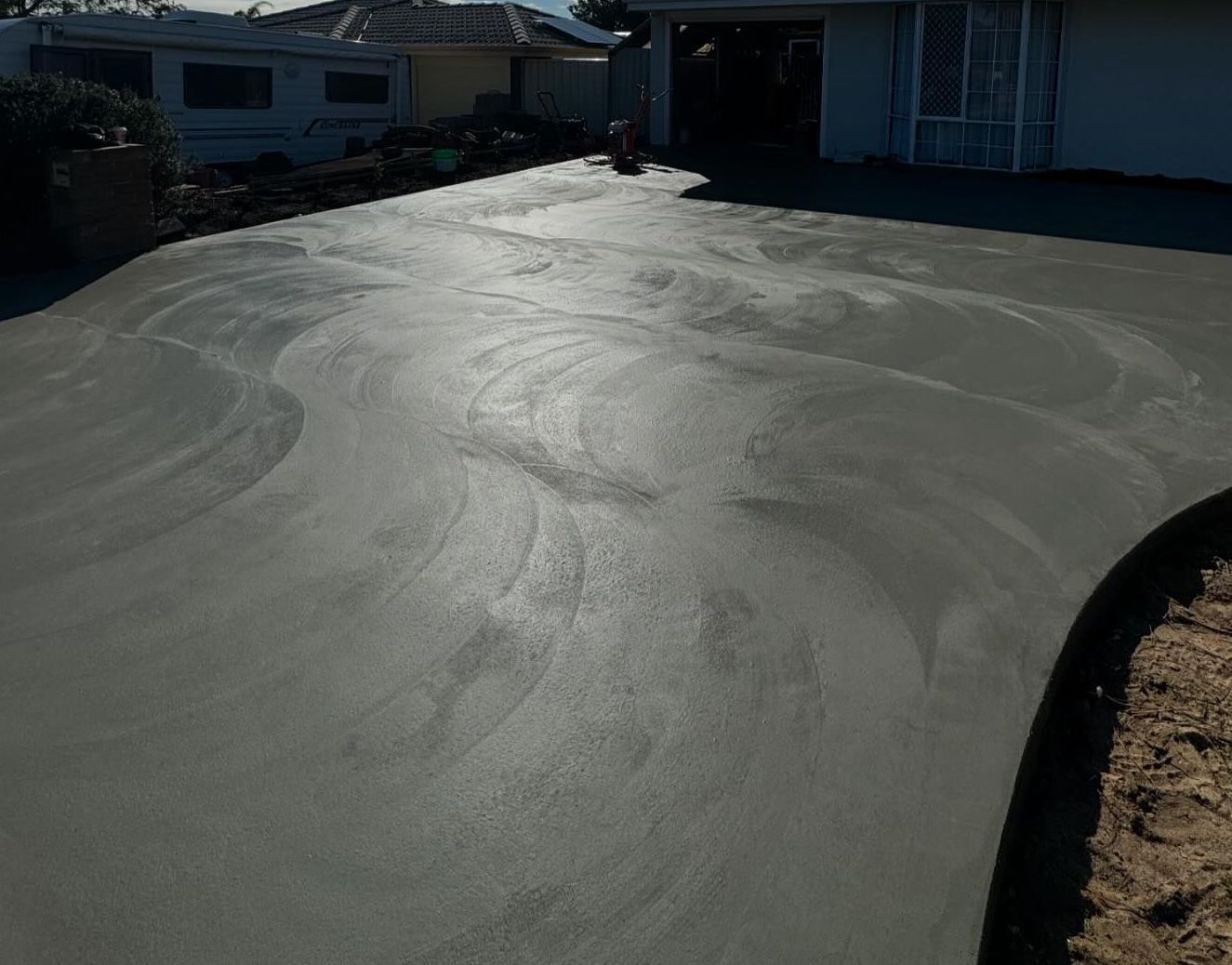 Freshly poured, wet concrete driveway, slightly curved, leading to a house with a garage.