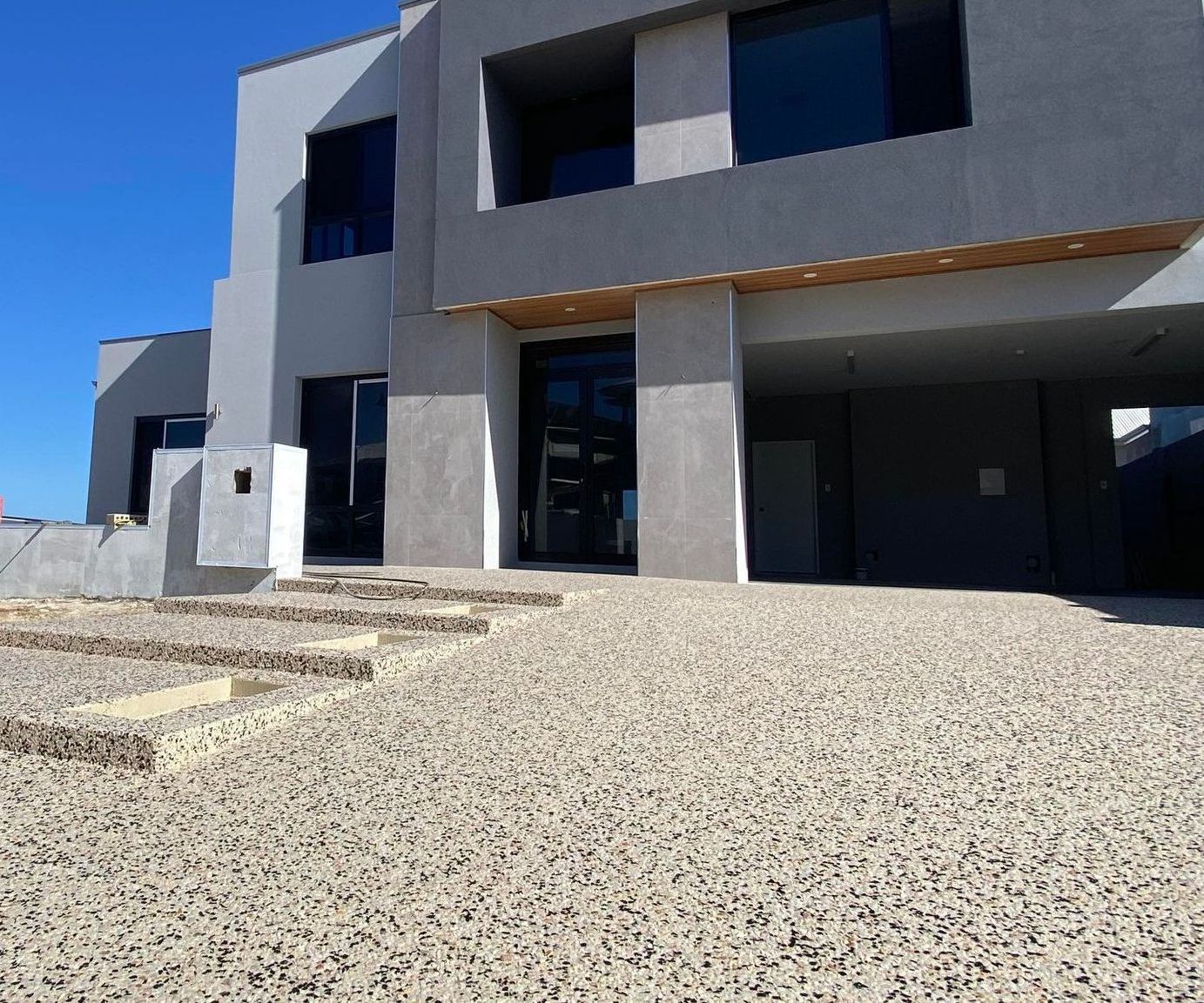 Exposed aggregate driveway with stairs in front of two storey home. 