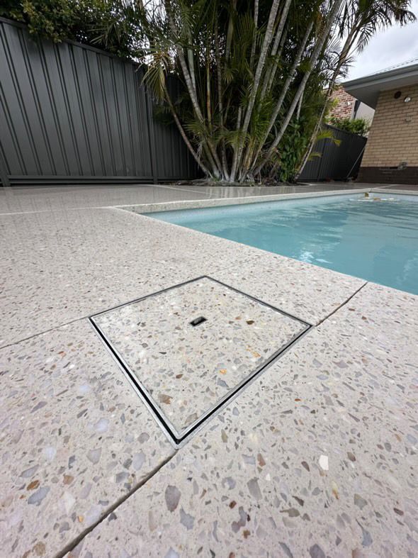 A swimming pool with a concrete drain cover on the side of it and new honed concrete pool surround