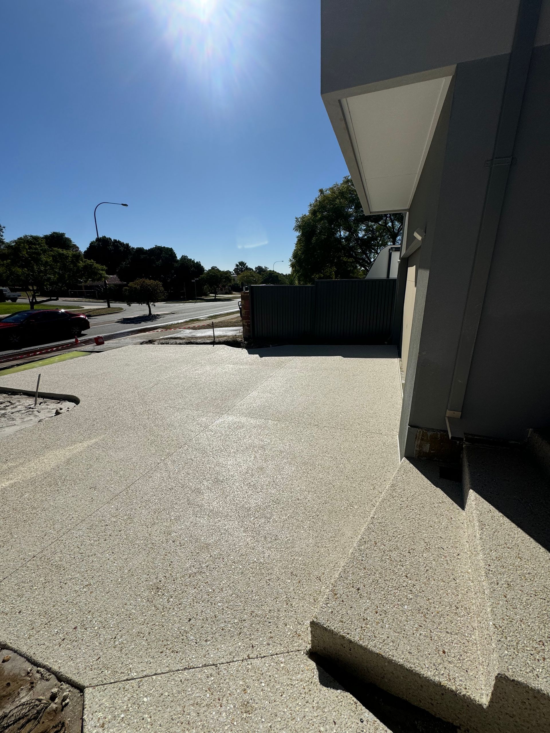 Concrete driveway beside a modern building, bright sunlight overhead.