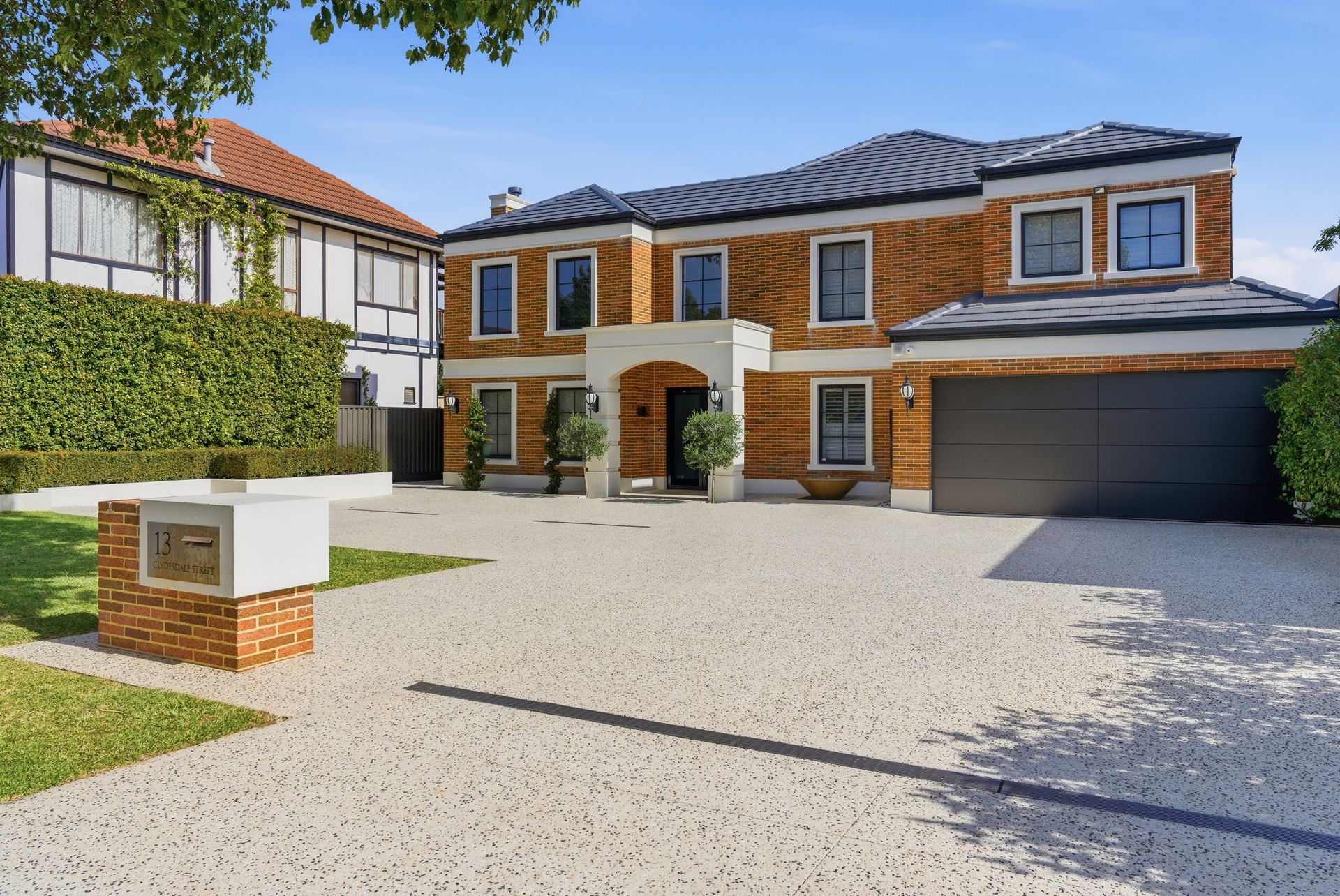 Exposed aggregate concrete driveway with drainage leading to front entrance of brick and tile home.