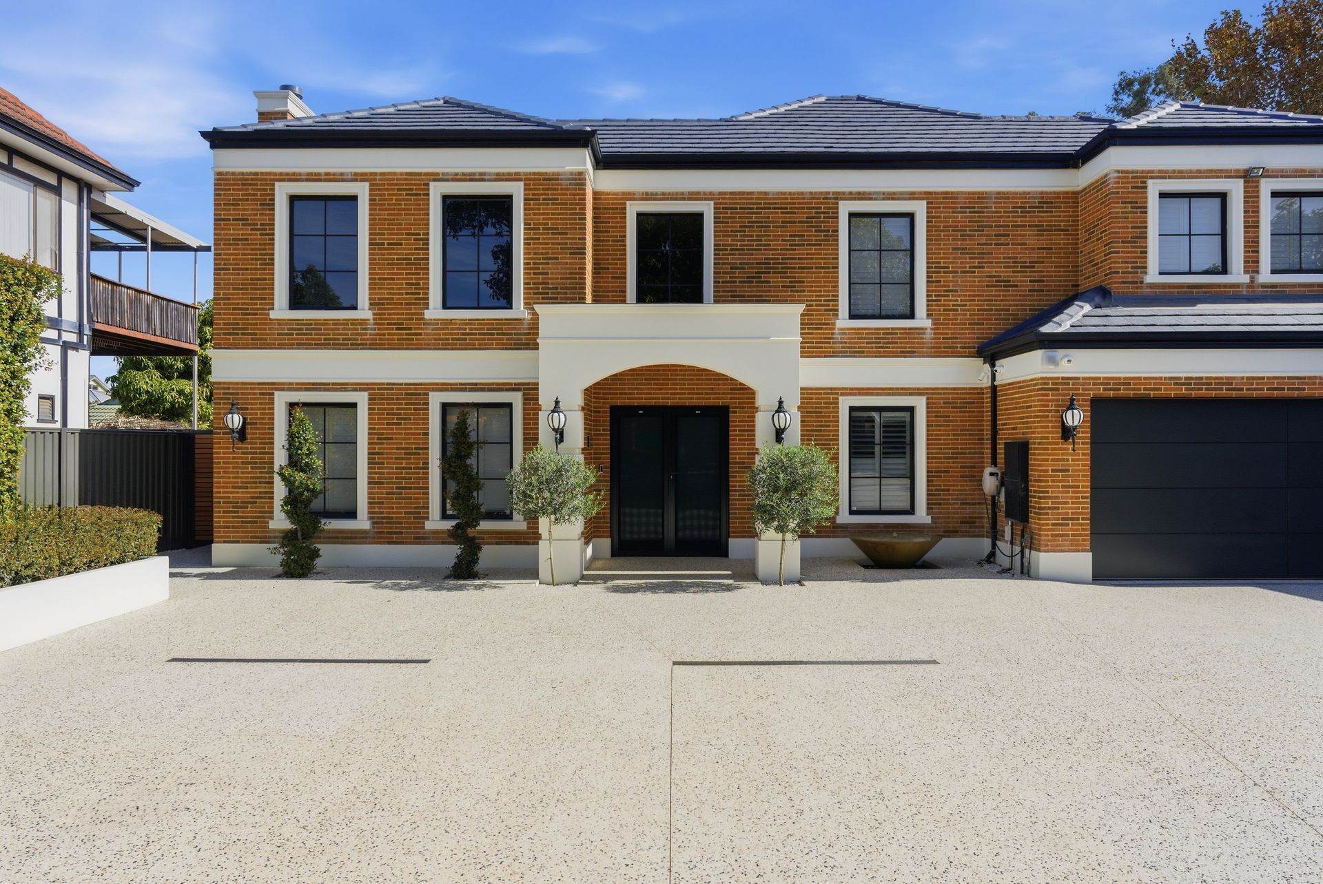 Modern two-story brick house with black garage door and gravel driveway under a clear blue sky