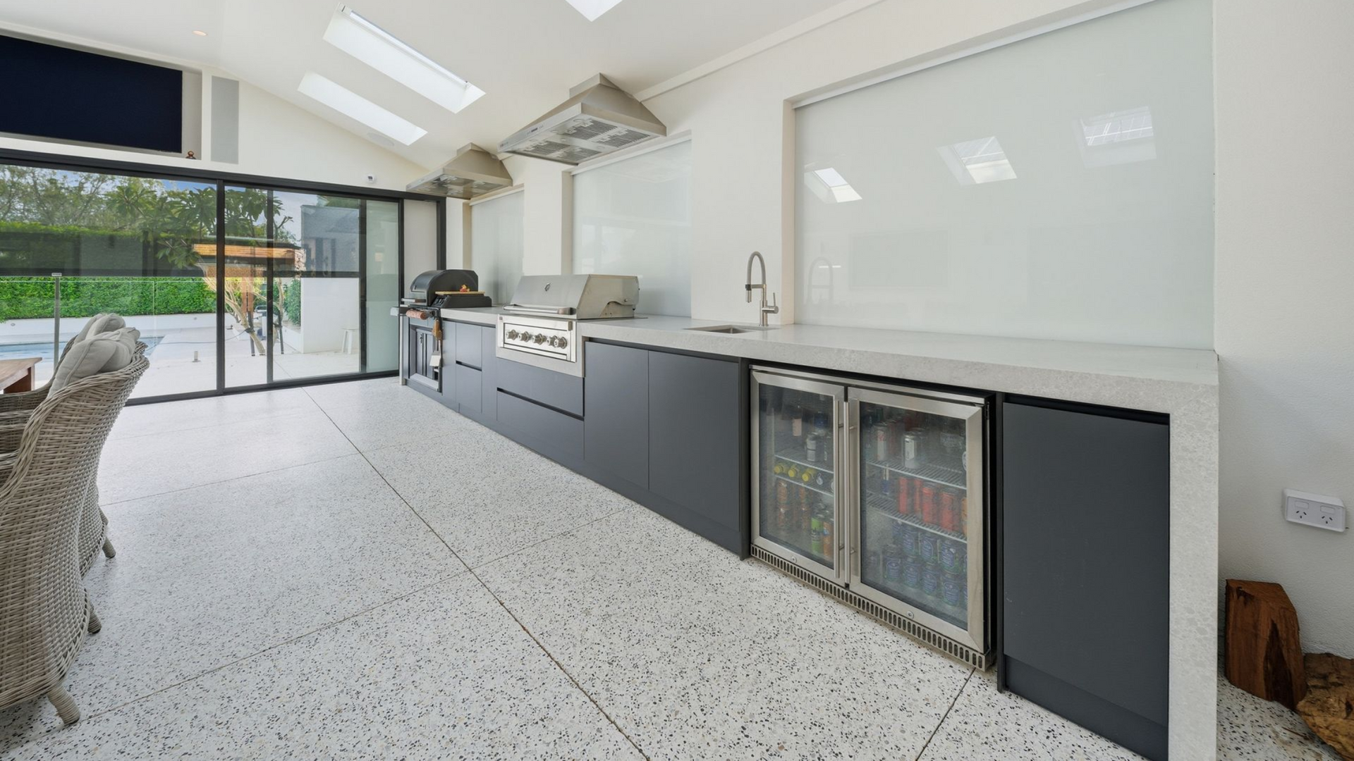 Honed concrete floor for indoor / outdoor kitchen with counter tops and bar fridge in Perth home.
