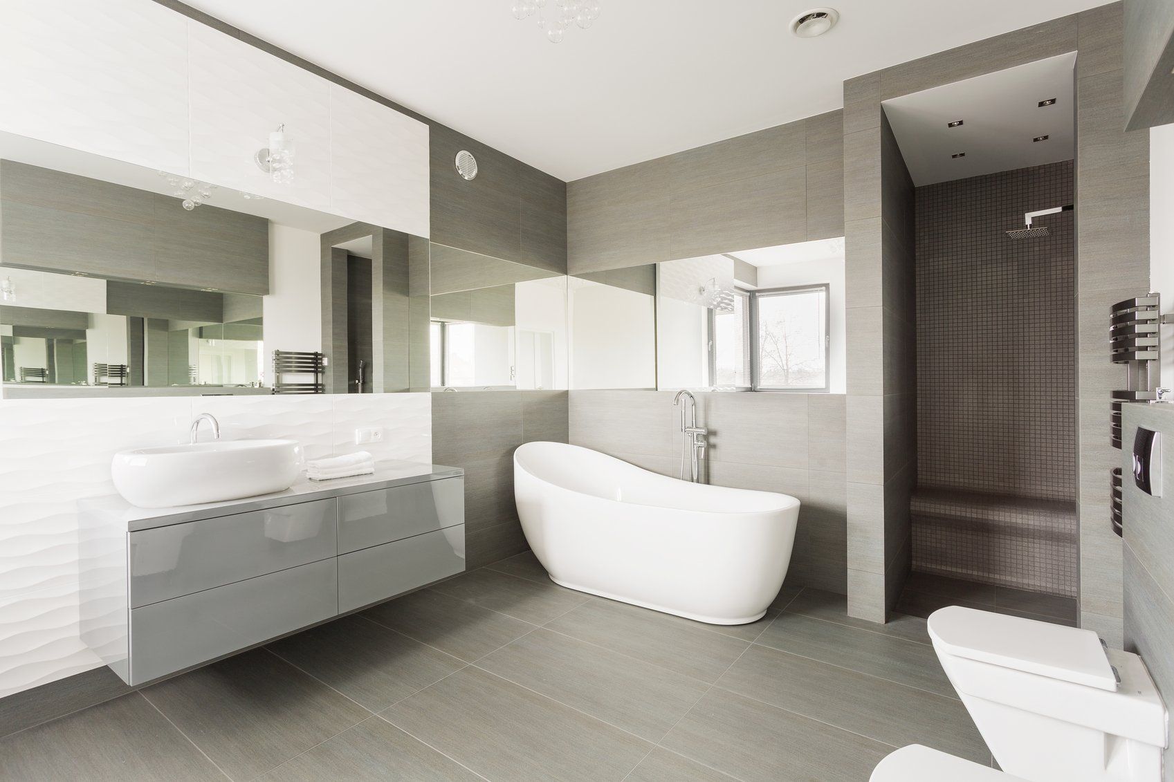 Modern gray bathroom with bathtub, shower, vanity with two mirrors, and a toilet.