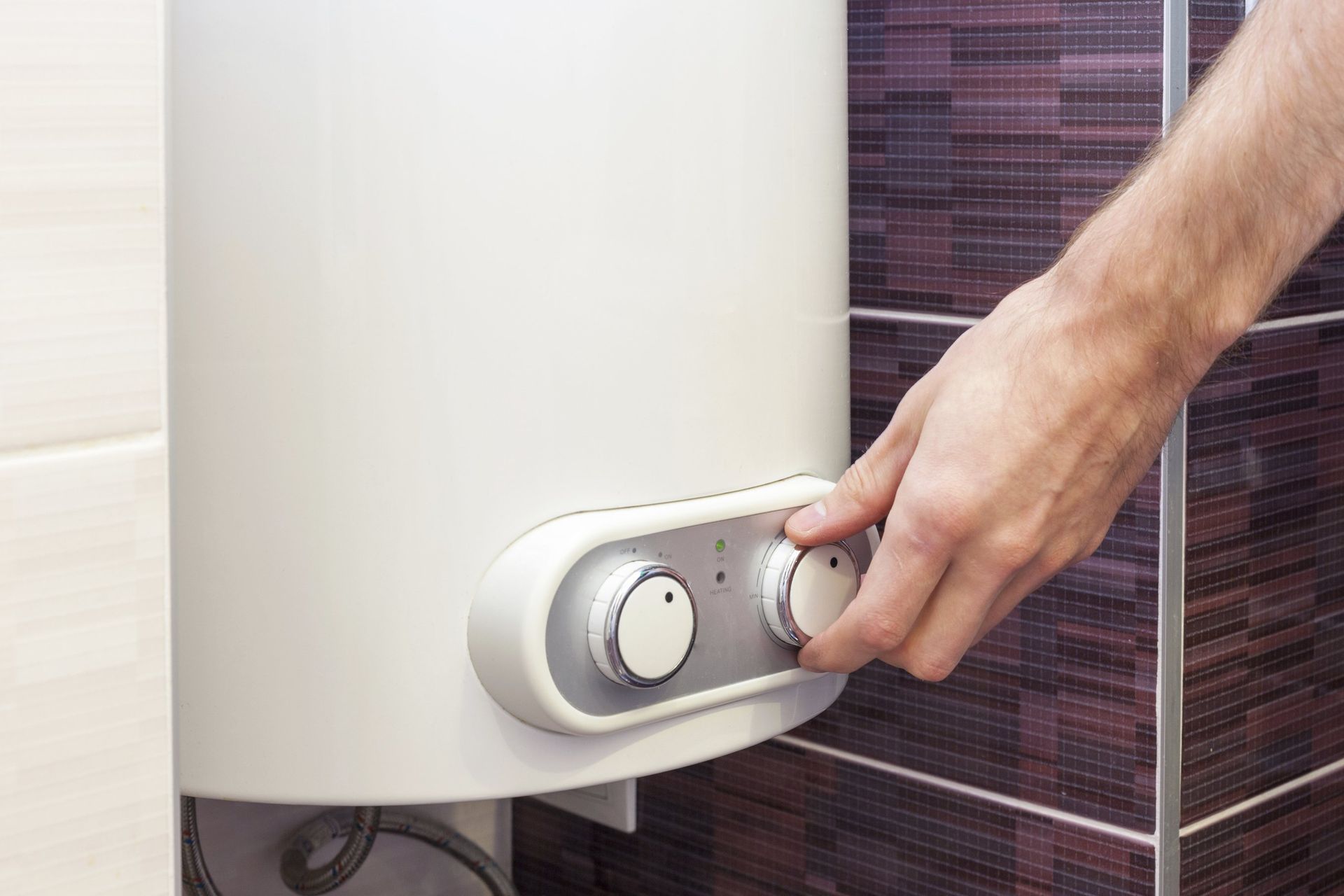 Person adjusting the dial on a white water heater, next to a tiled wall.