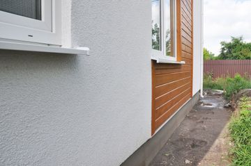 Extérieur d'un bâtiment avec un mur texturé blanc, un panneau en bois et une fenêtre blanche.