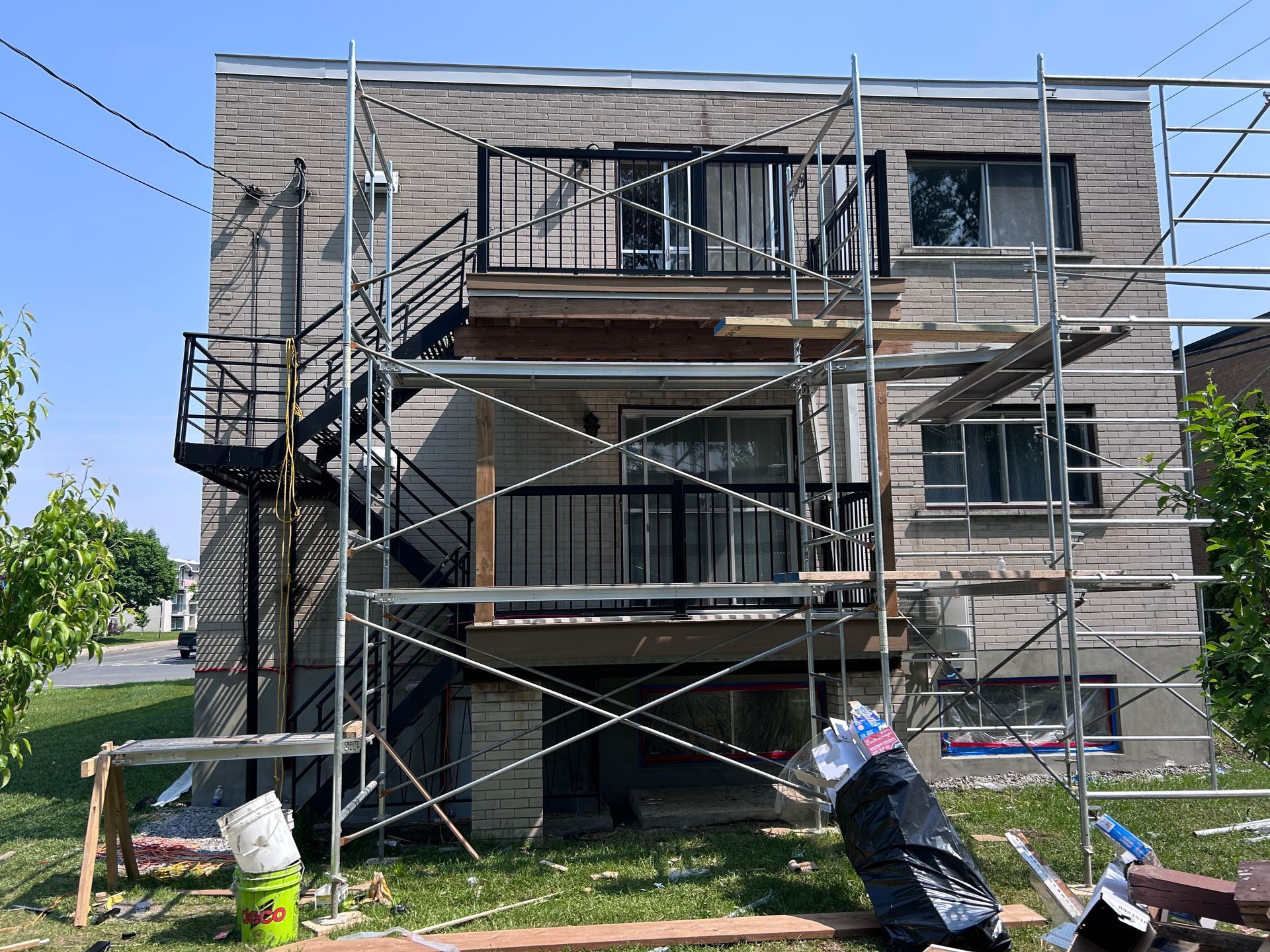 Bâtiment en briques de deux étages avec échafaudages, en cours de rénovation. Un escalier de secours en métal noir est visible à gauche.