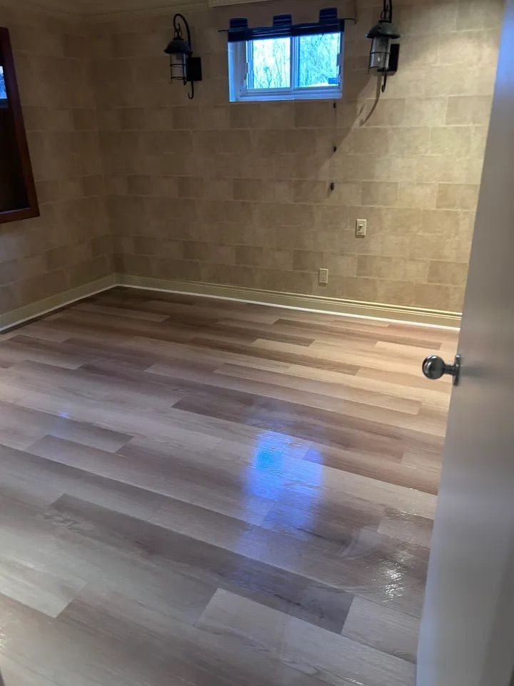 Pièce vide avec un nouveau parquet imitation bois et des murs carrelés. Une petite fenêtre et deux appliques murales sont visibles.