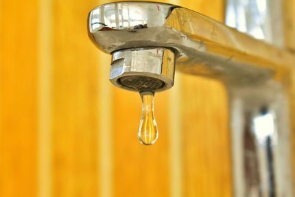 A close up of a faucet with a drop of water coming out of it.