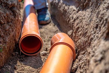 A person is installing drain pipes in a trench.