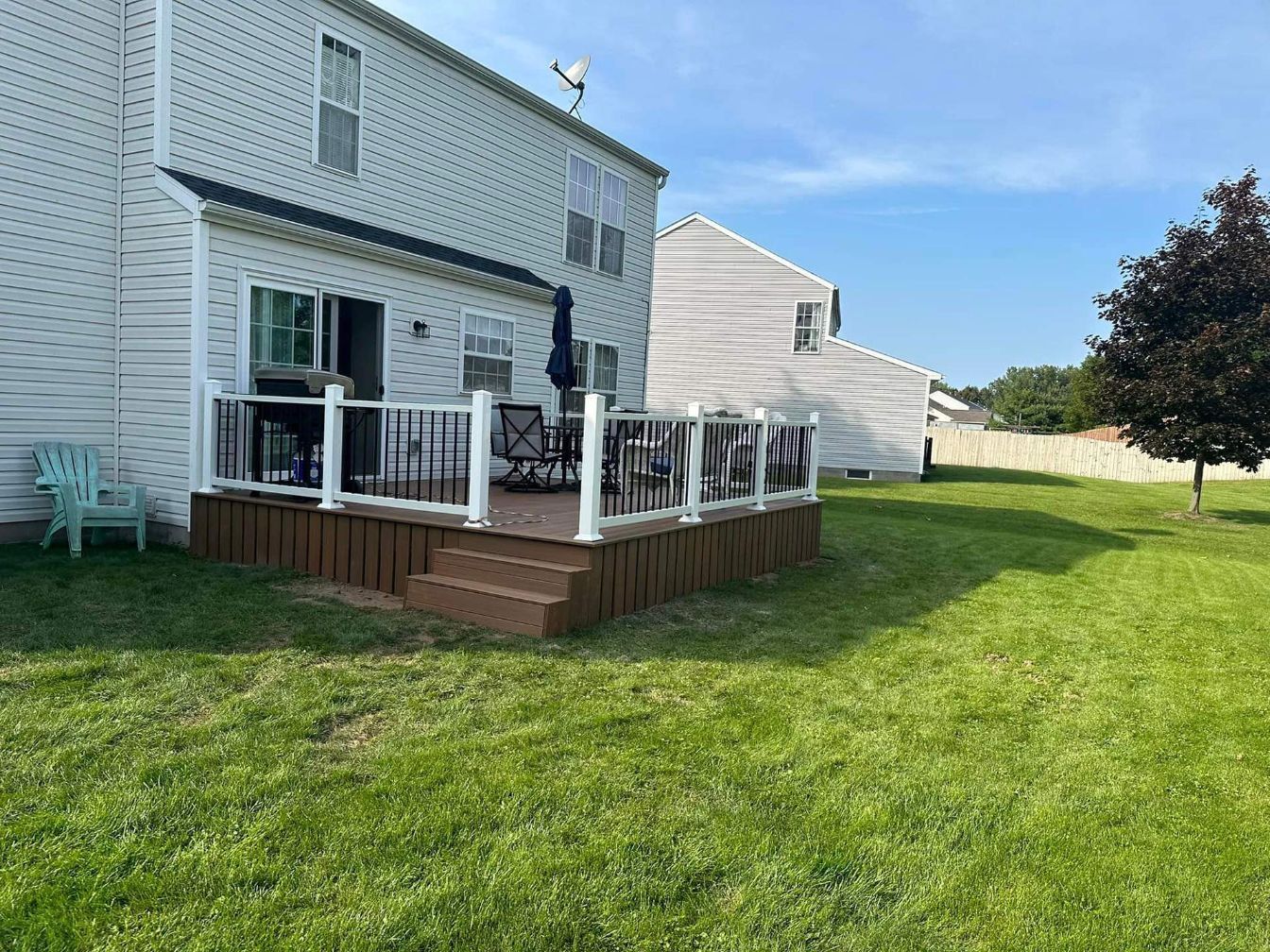 a deck with a white railing is in the backyard of a house .