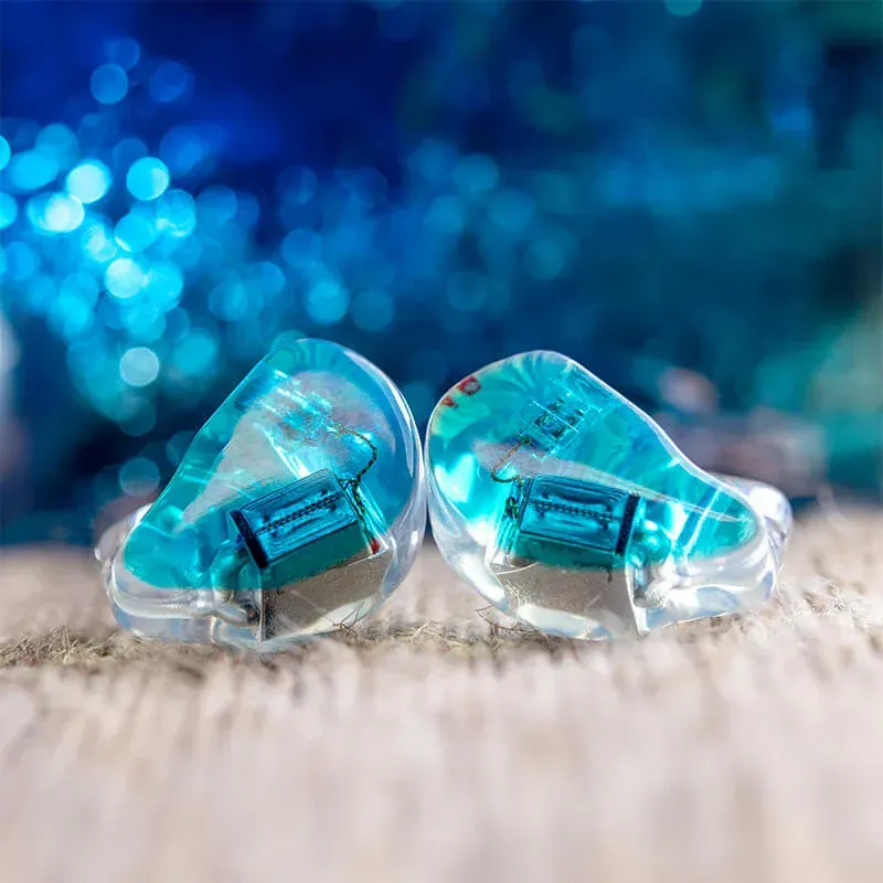 A pair of translucent blue, custom-molded in-ear monitors resting on a textured wooden surface against a blue bokeh backdrop.