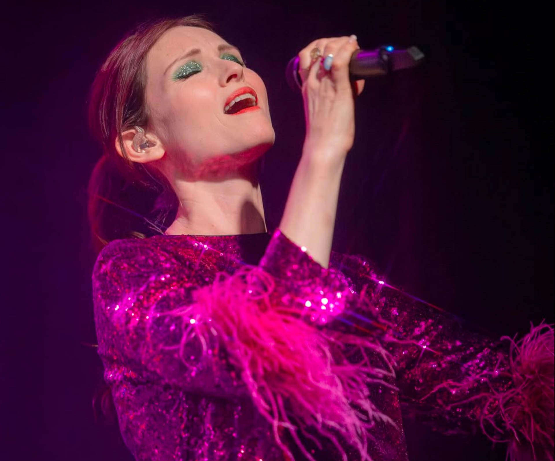 A singer  called Sophie Ellis-Bexter in a magenta sequined top with feathered sleeves performs into a microphone.