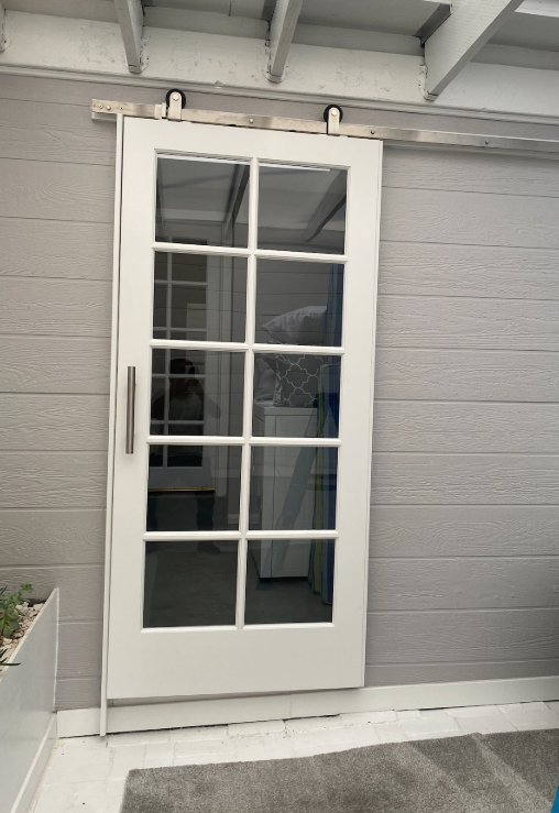 White sliding glass door on a gray wooden wall, with a stainless steel handle.