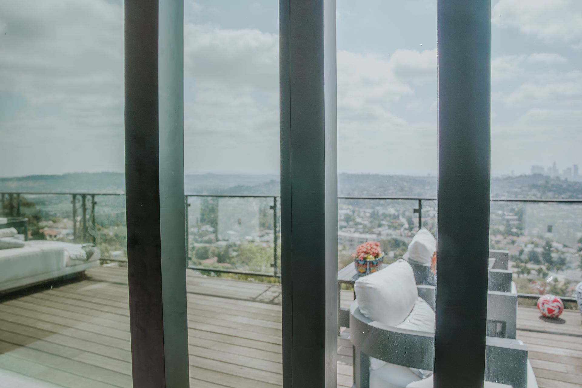 Outdoor patio with a city view seen through vertical beams; a gray chair and white cushions visible.