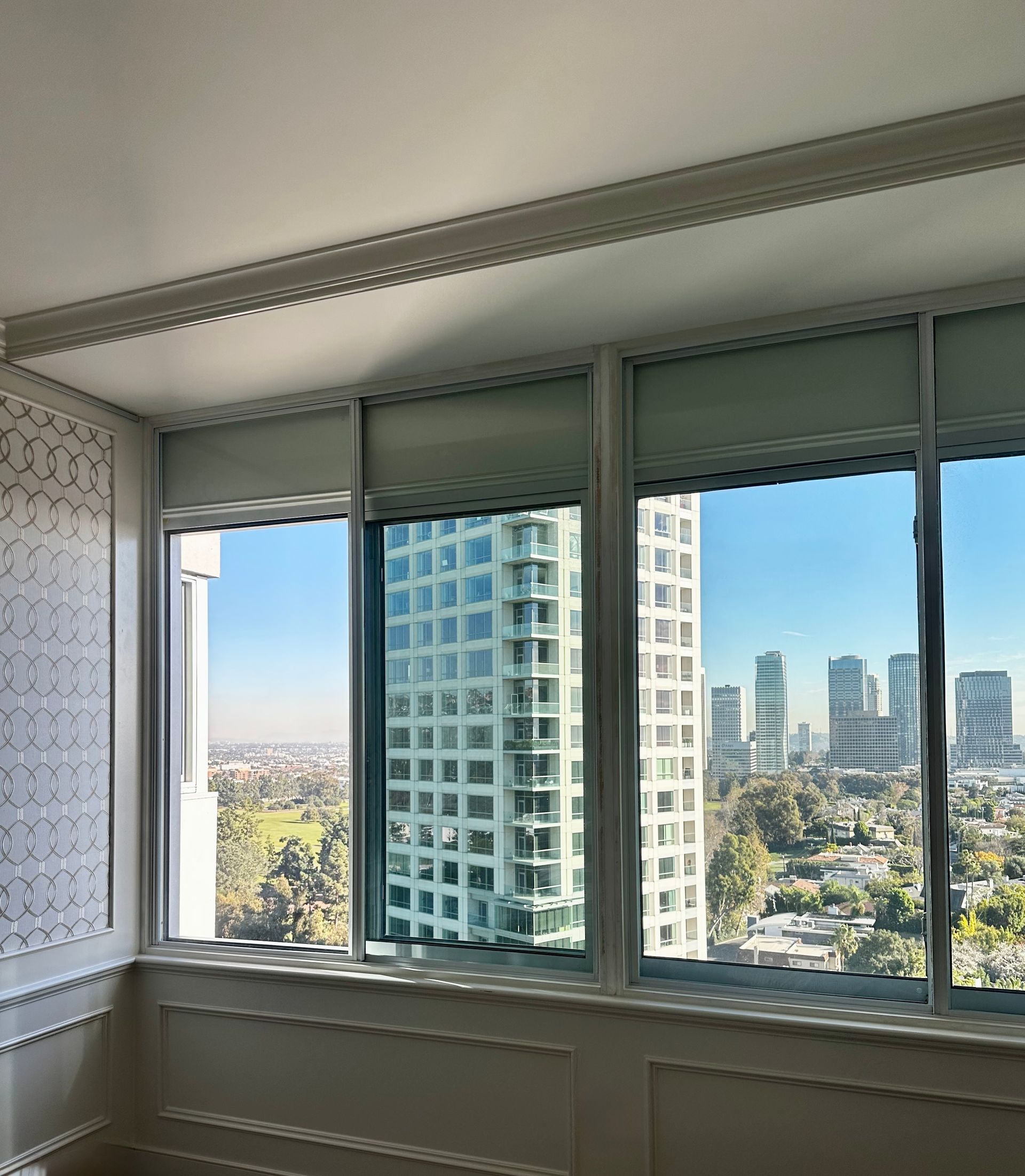 View through windows of city buildings, roller shades, white trim, with blue sky.