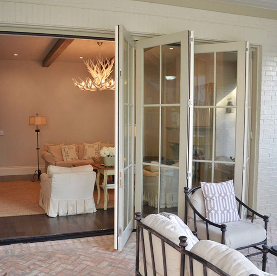 Folding glass doors open to a patio with seating, revealing a living room with a chandelier.