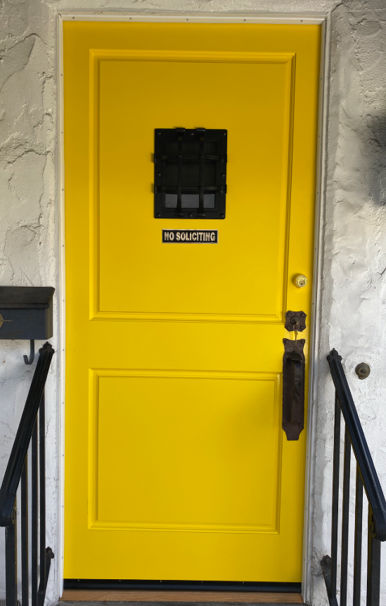 Yellow door with black window and hardware, address plaque, and black railings.