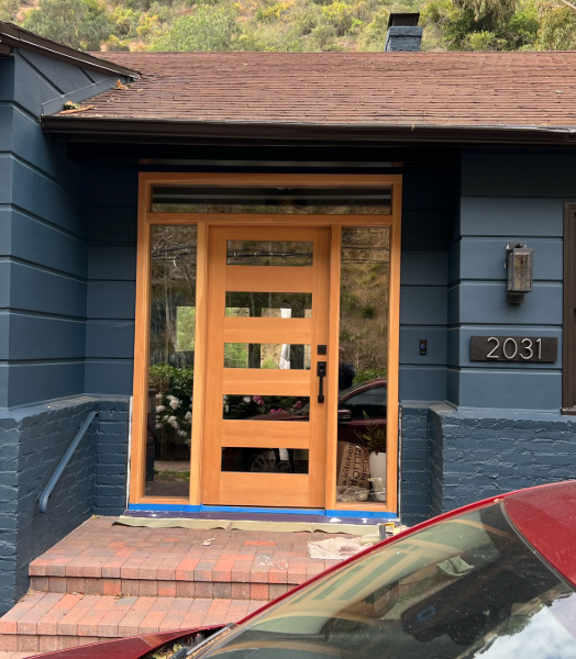 Blue house with wooden door and glass sidelights; red brick steps; car in foreground.