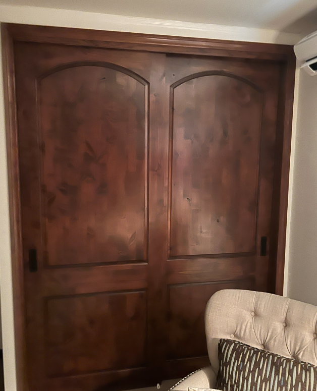 Dark wood closet doors with arched tops. A cream armchair with a patterned pillow is in front.